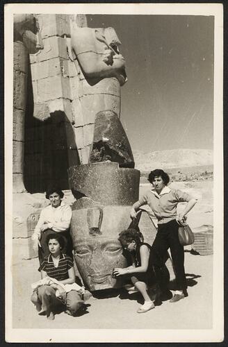 Four people pose outdoors with Egyptian archaeological pharoah statue.