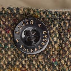 Dark button on brown trousers with maker's name and address. I. SATO TOORAK ROAD.