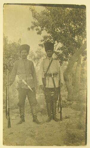 Two Kurdish men in military uniform standing under tree.
