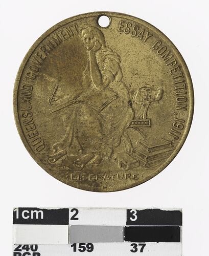 Round gold coloured medal with seated woman and text surrounding,