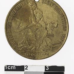 Round gold coloured medal with seated woman and text surrounding,