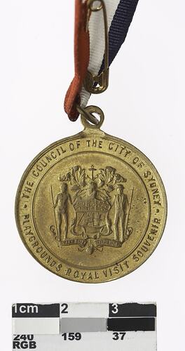 Round medal with coat of arms and text surrounding, red, white and blue ribbon attached.