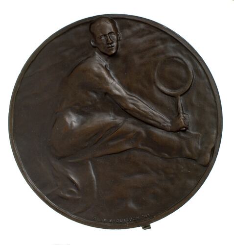 Round bronze medal with male tennis player moving right playing a backhand.