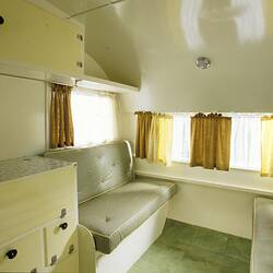 Caravan cream internal view, twin couch, storage cabinets, yellow and white curtains.