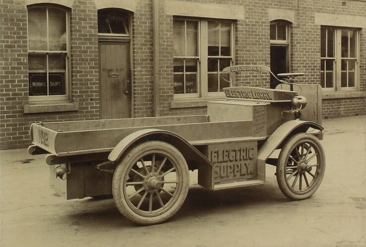 Baker electric lorry in front of brick building.