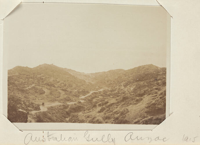 Hilly scrub covered landscape with two men walking on a dirt path on the left.