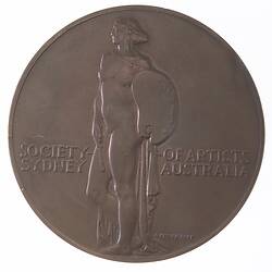 Round bronze medal with nude female figure and text.