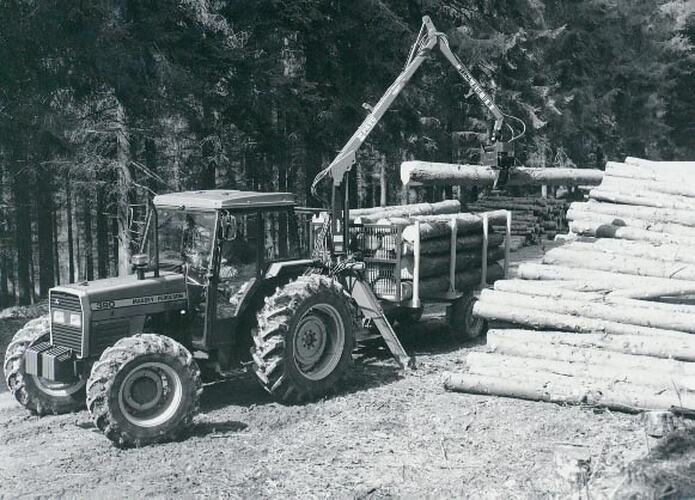 A tractor towing a forestry trailer being loaded with cut logs.