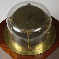 Detail of brass clock under glass dome on wooden octagonal box.