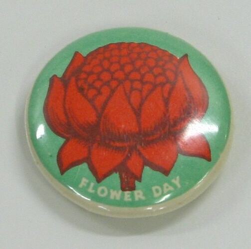 Badge with green background and red flower in centre with white writing below.