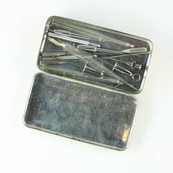 Metal rectangular box, lid off. Contains needles, trocars and three glass sheaths.