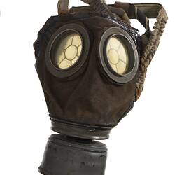 Dark leather mask with straps on back, clear eye lenses and grey metal air filter at base.
