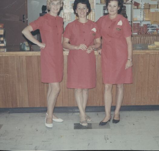 Three women in pink uniforms in shop.