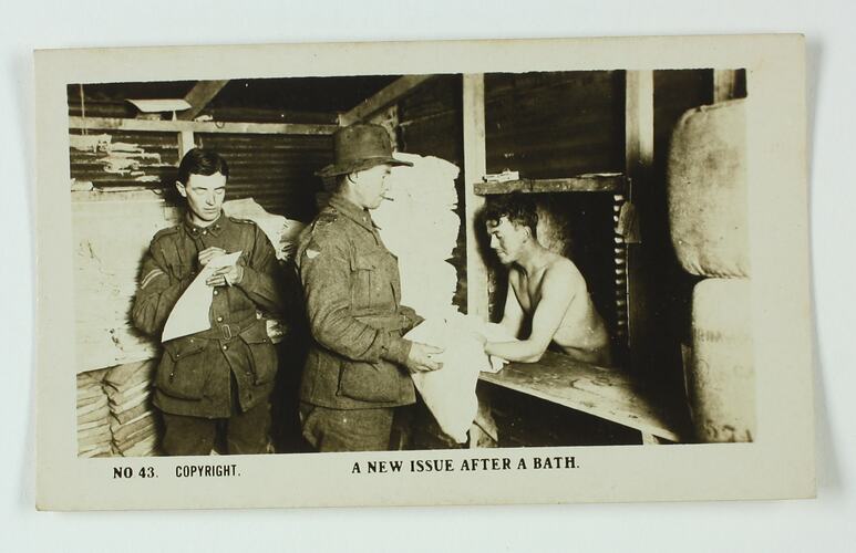 One shirtless soldier hands another soldier a towel, while a third soldier checks a document.