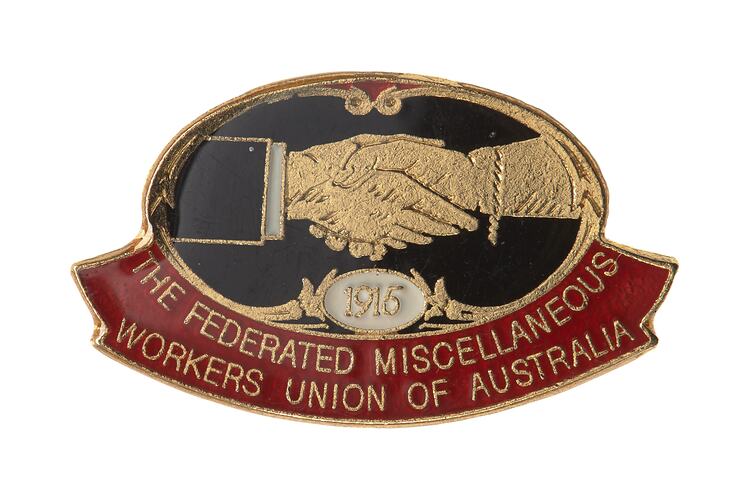 Enamel badge, blue oval over red banner. Two hands are shaking, one with suit cuff, other with bracelet.