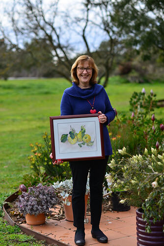 Woman holding a watercolour painting in a garden.
