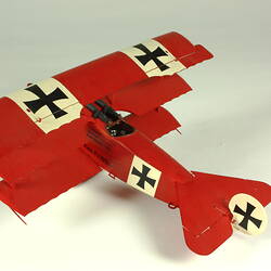 Red aeroplane model. White strip on top of wings with black cross. Left three quarter rear view.