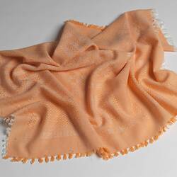 Orange and white woven baby blanket with geometric patterns and orange and white fringe around edges.