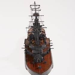 Wooden grey naval ship model with central tower, mast, mounted guns on wooden decks.
