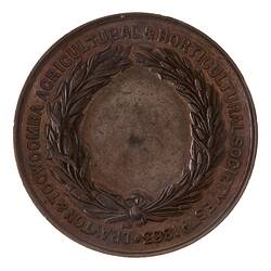 Round brown medal featuring wreath framed by border text.