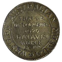 Medal with raised text in centre. Framed by beaded border and raised text around edge.