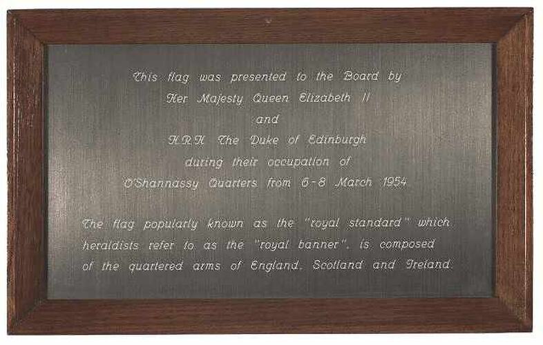 Metal plaque engraved with text, set in wood frame.