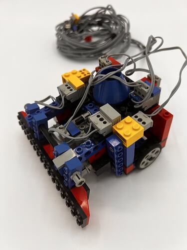 Multi-coloured LEGO robot with black wheel and grey cable.