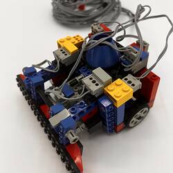 Multi-coloured LEGO robot with black wheel and grey cable.