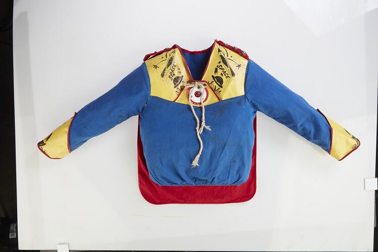 Child's long sleeve blue top with yellow cuffs and yellow/blue patterned yoke. Red cape hangs at back.