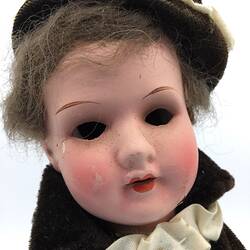 A doll dressed in a cream tunic with a red cross, cream pants and a dark cloak