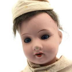 The face of a doll dressed as a Benedictine Monk in a pale brown cassock and cap
