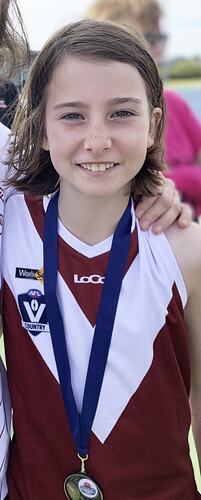 Half portrait, girl wearing maroon and white v design football jumper with blue ribboned medal around neck.