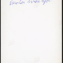 White back of rectangular photograph. Handwritten text in blue ink.