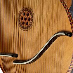 Detail of central section of timber stringed instrument. Pale wood with black laquered timber detail. Multi stringed. Central sound hole has seven small holes.