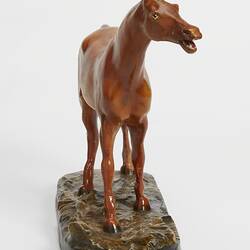 Plaster moulded, hand painted brown horse with a black base. Front view. Horses head faces right.