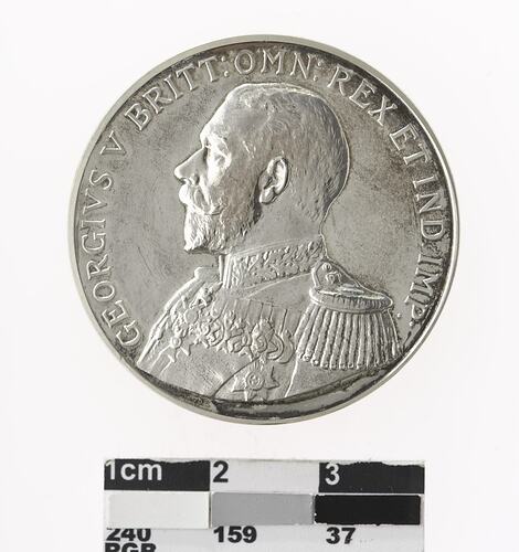 Round silver coloured medal with profile of a man and text surrounding.