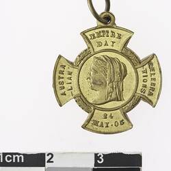 Cross -shaped, gold coloured medal with profile of a woman and text surrounding.