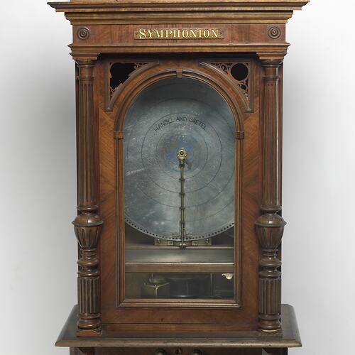 Detail of upright decorative wooden cabinet, a musical box. Contains circular disc.