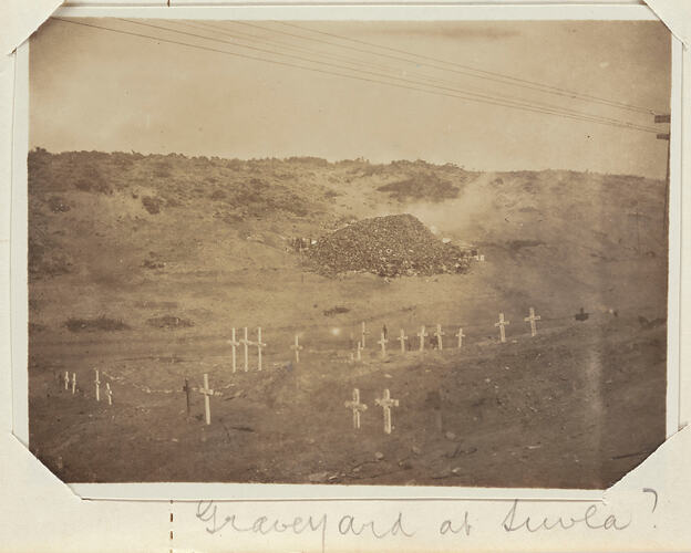 Sloping scrub covered landscape with graveyard in valley at bottom.