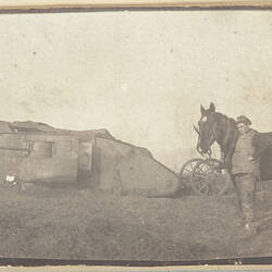 Tank in the middle of a field, with a soldier holding a horses by its bridle in the right foreground.