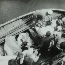 View from above of a lifeboat with multiple people assisting a wounded man laying at bow of boat.