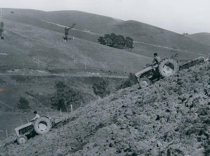 2  tractors with mouldboard ploughs operating on a steep hill.