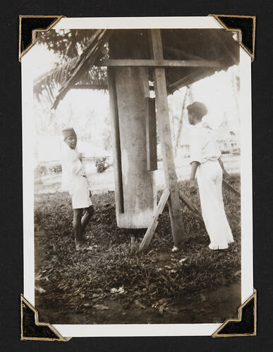 Two men standing next to wooden construction made of upright log and wood and roof.