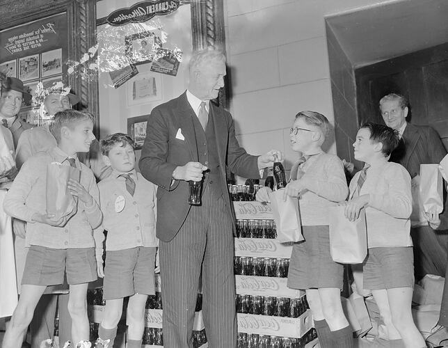 Man handing out bottles of drinks to children.