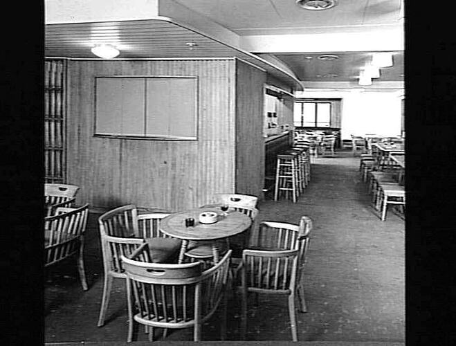 Ship interior. Wooden round chairs and tables. Bar in background with stools.