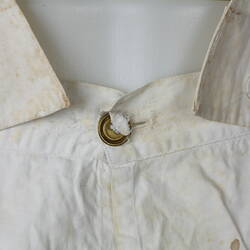 White cotton garment, with fabric straps buttoned to waist, close up view.