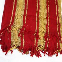 Detail of rectangular scarf striped red and yellow with gold thread fabric, fringed at the end.