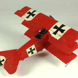 Red aeroplane model. White strip on top of wings with black cross. Right three quarter rear view.