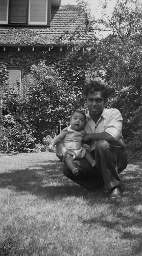 and child kneeling outside house on lawn.