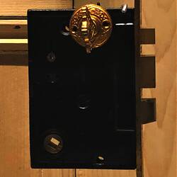 Rectangular metal door lock and latch with gilt faceplate featuring inset decoration. Lock has three bolts.